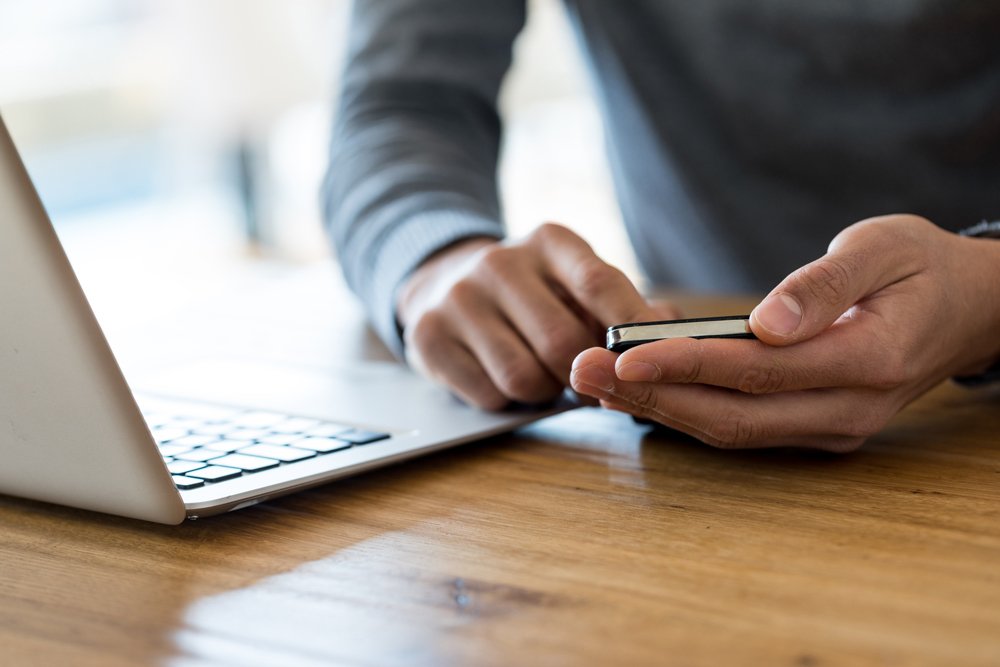 14 Closeup of hands holding mobile device swiping with finger on wooden table with laptop